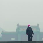 Woman wearing a mask walks outside the old palace museum on a hazy day in Shenyang